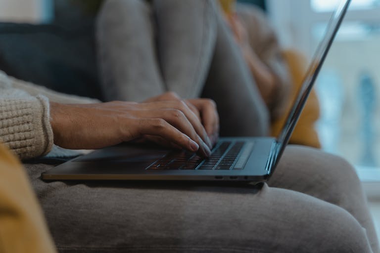 A close-up view of a person's hands typing on a laptop, capturing a cozy and modern indoor setting.