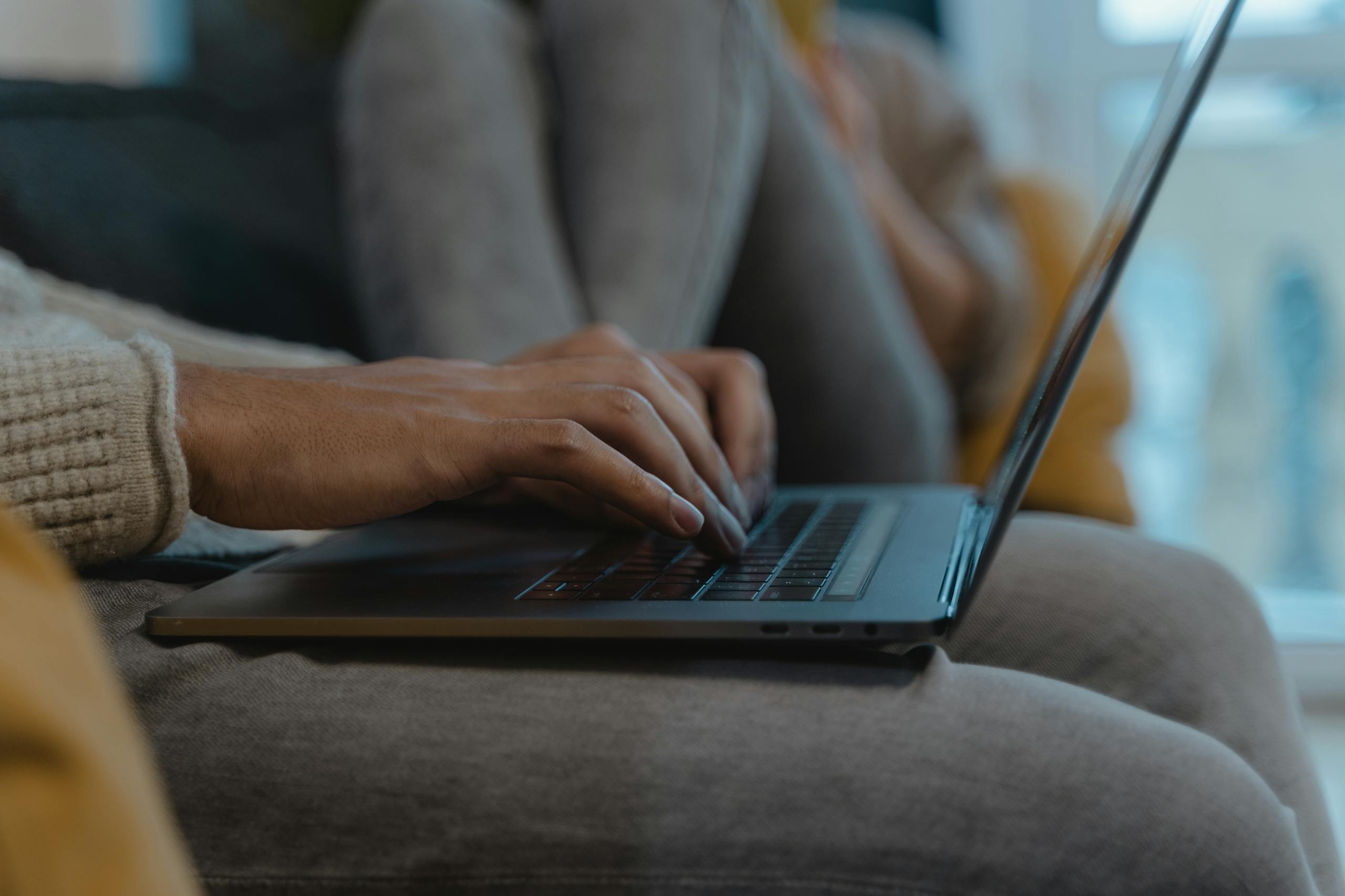 A close-up view of a person's hands typing on a laptop, capturing a cozy and modern indoor setting.